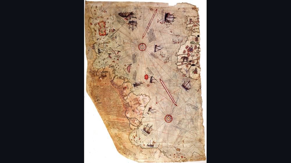 Weathered parchment fragment of the 1513 Piri Reis map showing coastlines, compass roses and small ships.