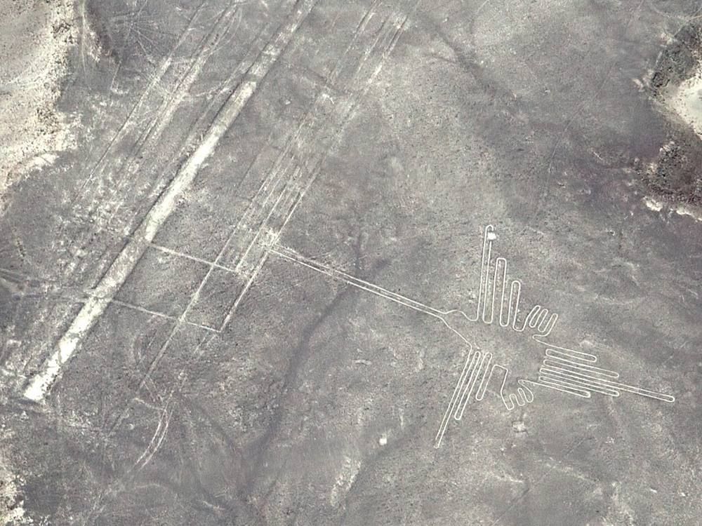 Aerial photo of long straight lines and a hummingbird-shaped geoglyph on the Nazca plain.