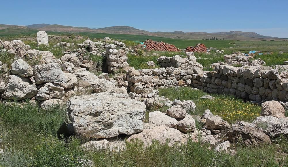 Low stone wall foundations of an excavated building on a grassy mound.