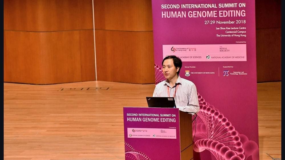 A man at a podium with a laptop on a wooden stage in front of a pink summit banner reading Second International Summit on Human Genome Editing.