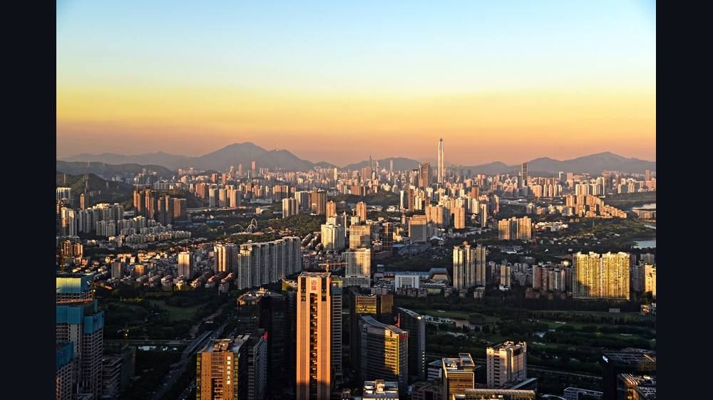 A wide view of a dense city of high-rise towers at sunset with hills in the distance.