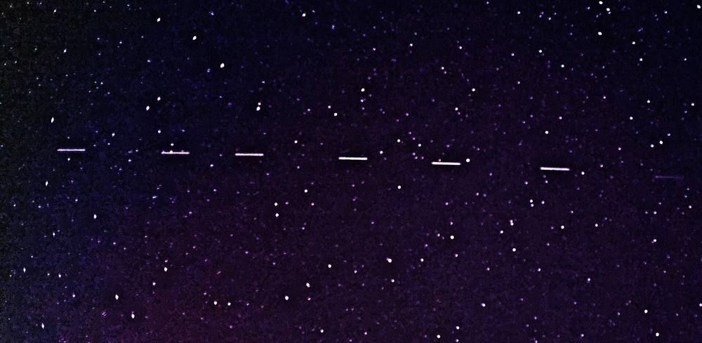 Six small bright dashes in a line across a dark star-filled sky, the satellites of a Starlink train.