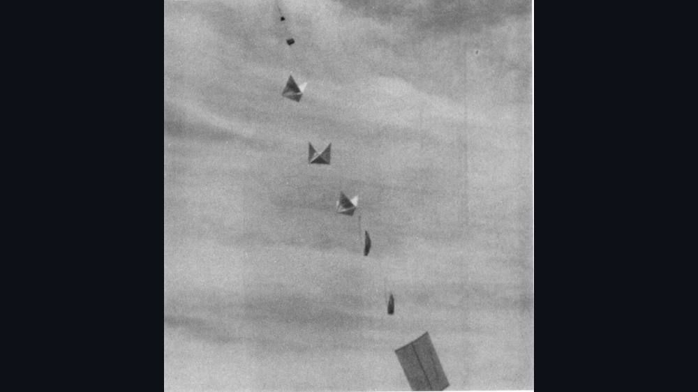 Black-and-white photograph of a long balloon train rising with small radar reflectors hanging below.